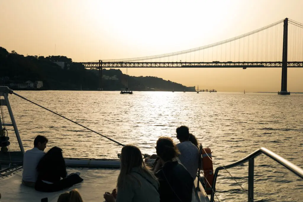 People enjoying the sunset on a boat under Lisbon's bridge
