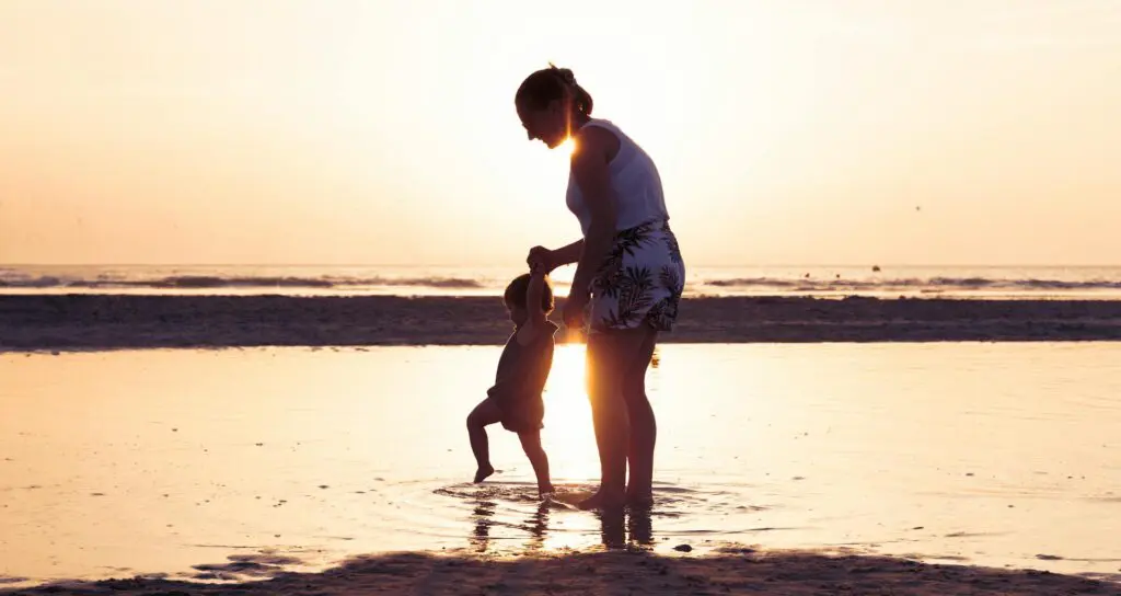 Mãe a brincar com o filho no mar ao nascer do sol