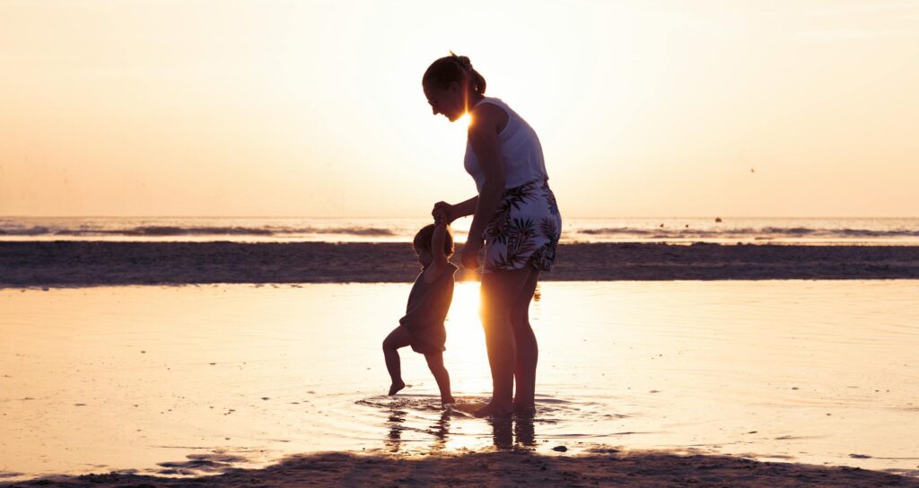 Mom playing with child in the sea at sunrise