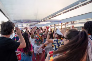 Un grupo de personas bailando y sosteniendo bebidas en un barco de fiesta navegando por el río Duero en Oporto durante una hermosa puesta de sol.