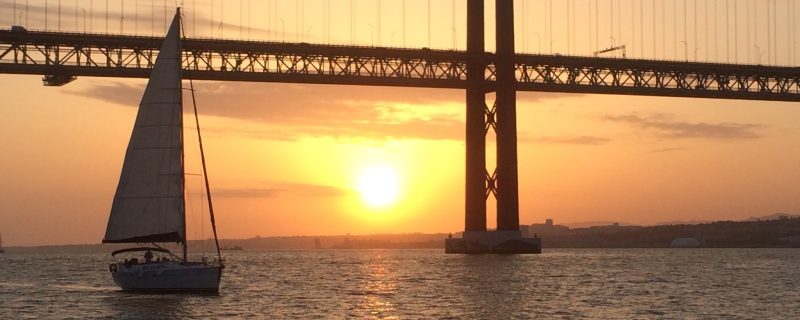 sailing boat under the 25th of April Bridge in Lisbon during sunset