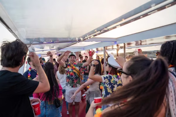 A group of people dancing and holding drinks on a party boat sailing on the Douro River in Porto during a beautiful sunset.