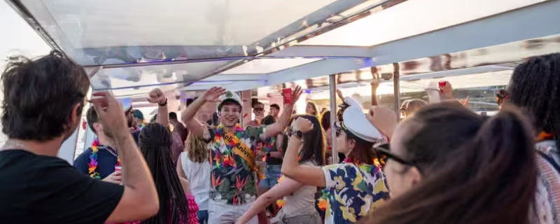 A group of people dancing and holding drinks on a party boat sailing on the Douro River in Porto during a beautiful sunset.