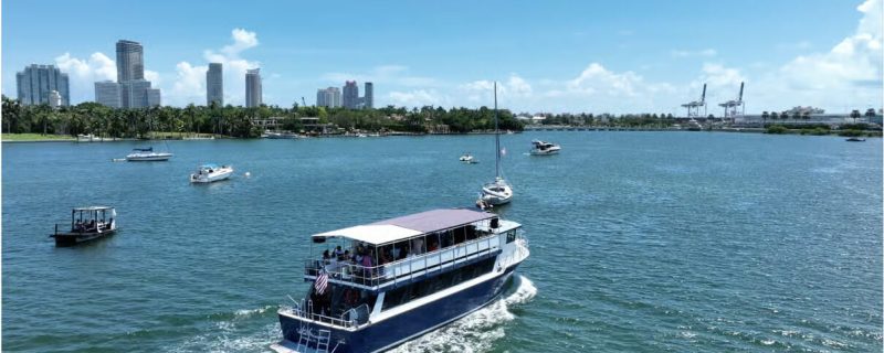 A large bi-level sightseeing boat cruising through the blue waters of Biscayne Bay.